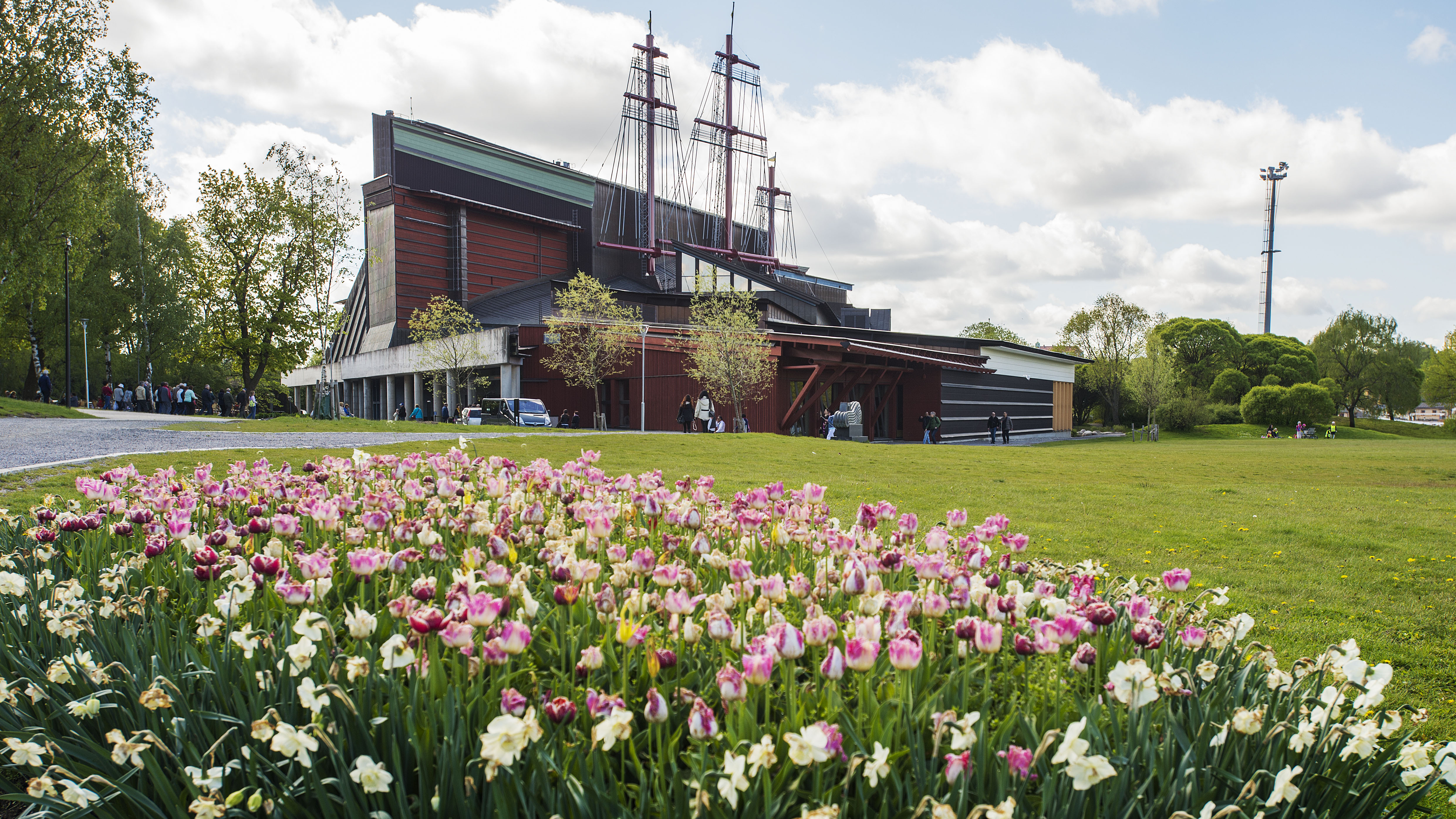 Vasamuseet, en hög byggnad med master på taket, i sommarväder med tulpaner i förgrunden. 